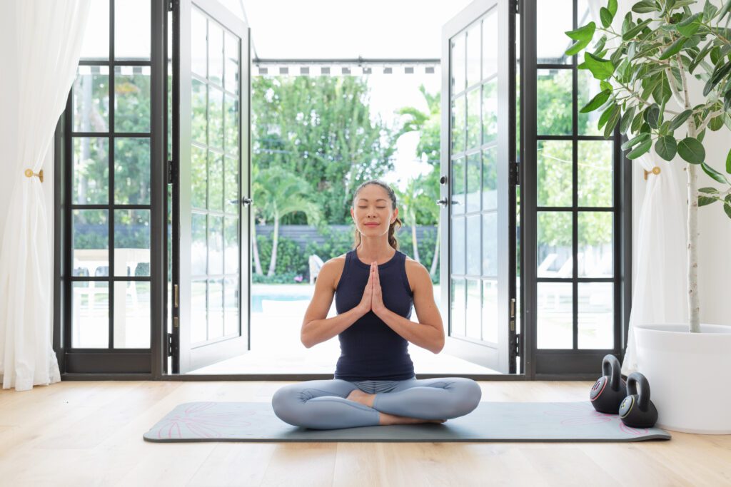 Homeowner practicing yoga in bright living space with open French doors, highlighting natural light and indoor-outdoor comfort from quality window and door design