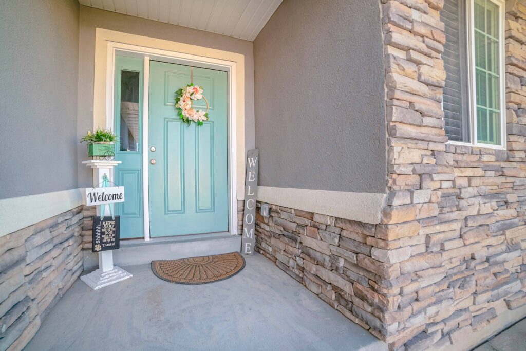 Teal front entry door with decorative wreath, sidelights, and stone exterior, creating a welcoming modern home entrance
