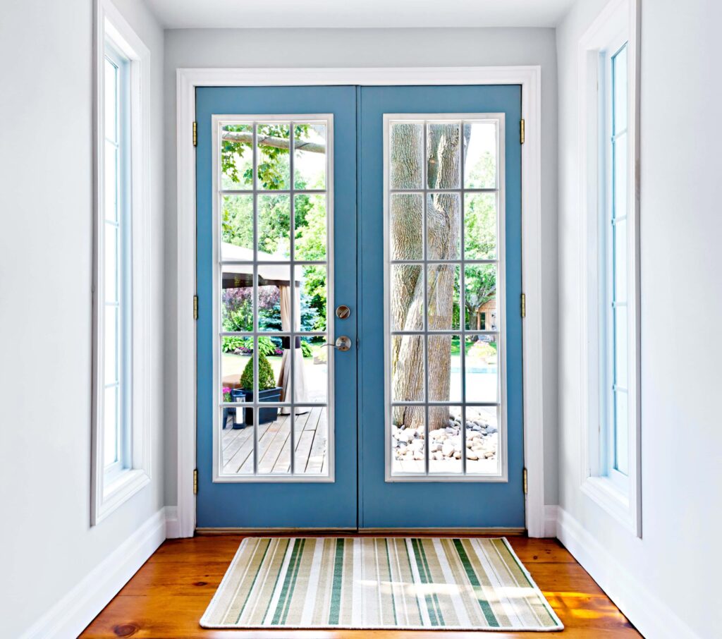 Blue double front doors with divided glass panes, highlighting classic style, outdoor views, and bright, welcoming interior entry