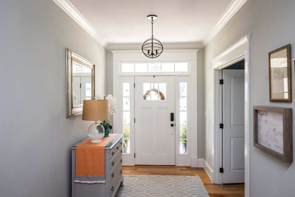 Bright interior foyer with white front door, sidelights, and transom window, featuring clean trim details and natural light