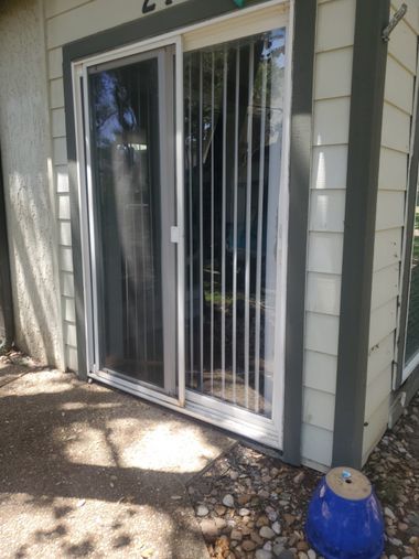 Outdated sliding glass patio door with worn frame and vertical blinds, showing signs of age and reduced efficiency before replacement