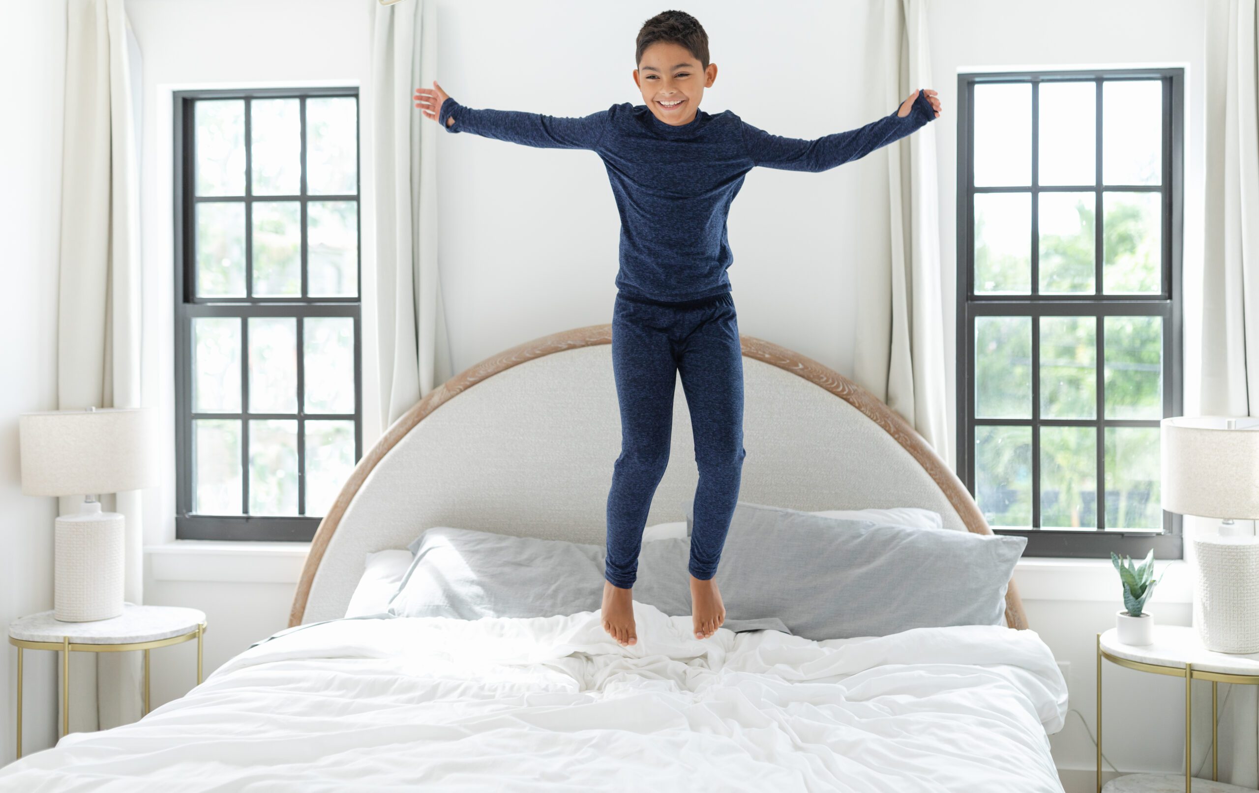 Child jumping on bed in bright bedroom with new energy-efficient windows, showcasing improved natural light and comfort from Wallaby Windows