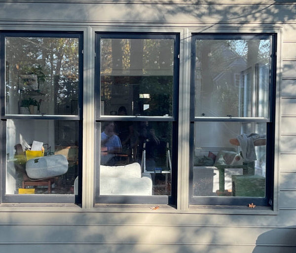 Older multi-pane windows on gray house before fixed window installation